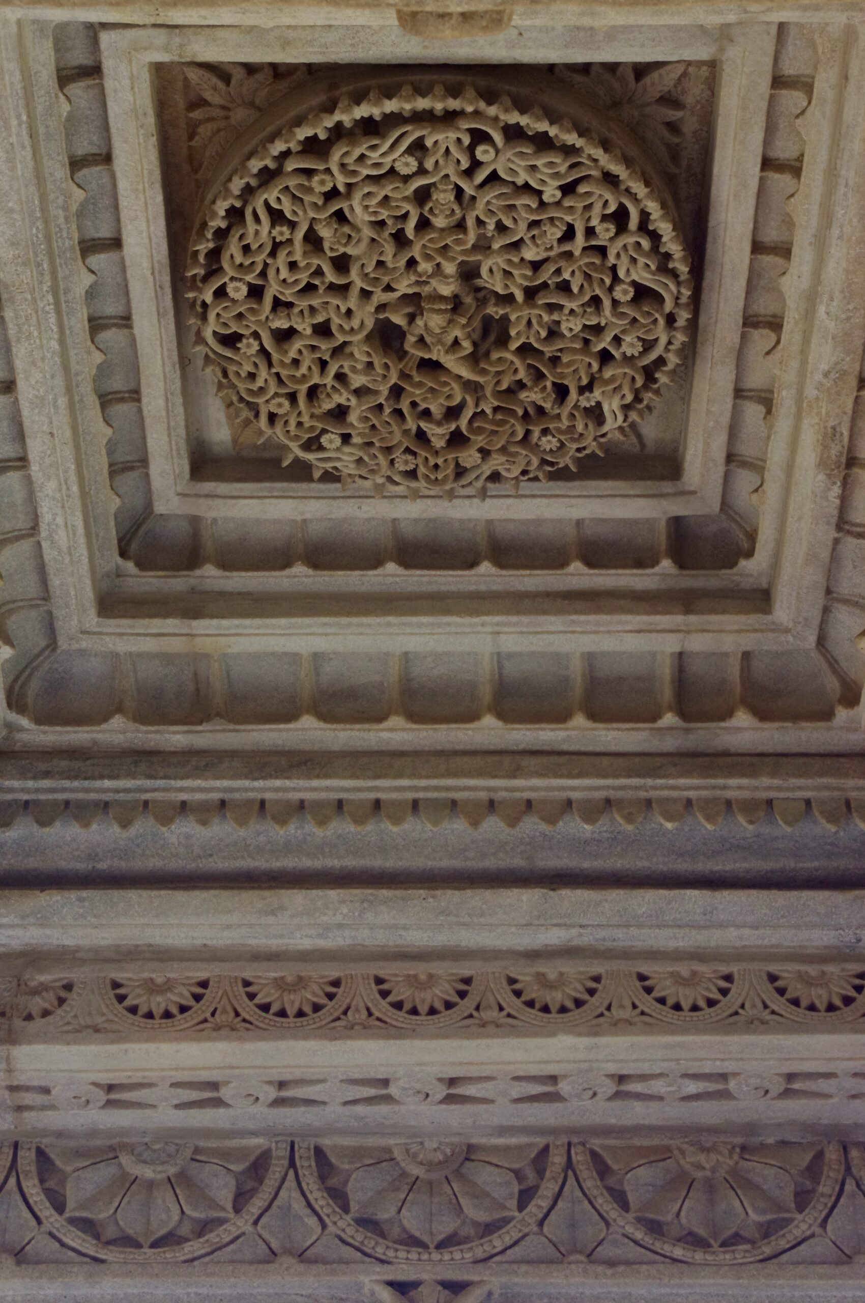 An intricately carved stone ceiling in a historic building. The central circular pattern features detailed floral and geometric designs, surrounded by additional ornate carvings. The craftsmanship displays deep textures and symmetrical arrangements.